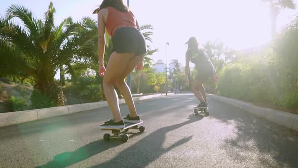 Two Female Friends on Skateboards Rides Downhill at the Resort Having Fun Moving and Smiling. Road