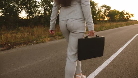 Businesswoman Walking Down Road with a Black Briefcase in Her Hand