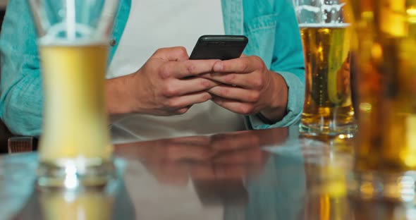 Man is Typing a Message on a Smartphone in a Bar While a Glass of