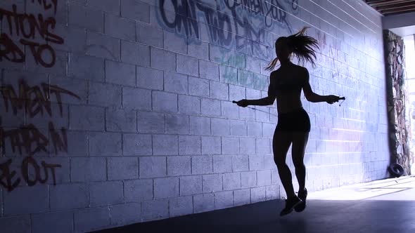 Silhouette of a young woman jump roping in a gym.