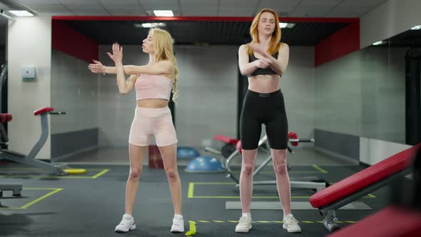 Wide Shot Portrait of Two Confident Young Caucasian Women Stretching Hands Training in Gym