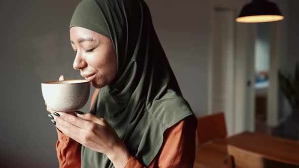 Happy Muslim woman wearing hijab sniffing tea