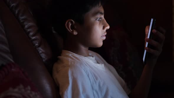 Teenage Boy Sitting on Sofa Using Smart Phone at Night