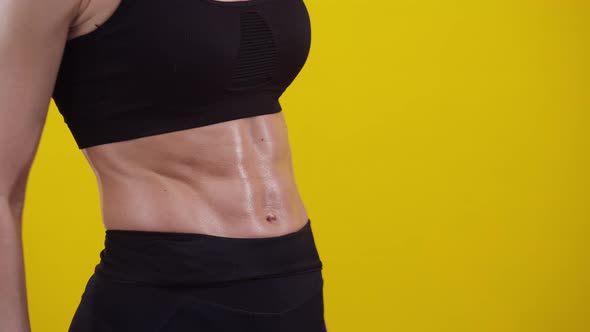 Woman Holds a Bottle of Water in Hand and Shows on the Muscular Belly a Finger Closeup