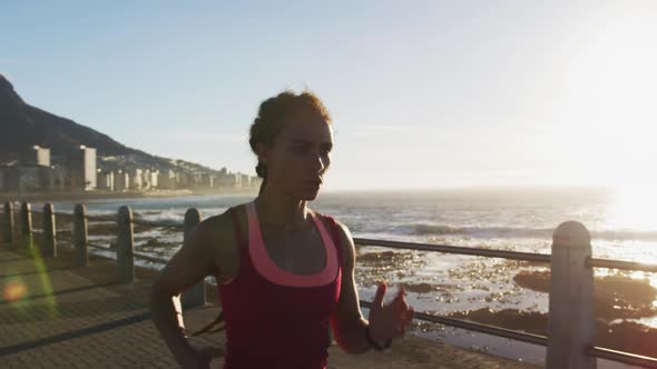 African american woman running on promenade by the sea at sundown