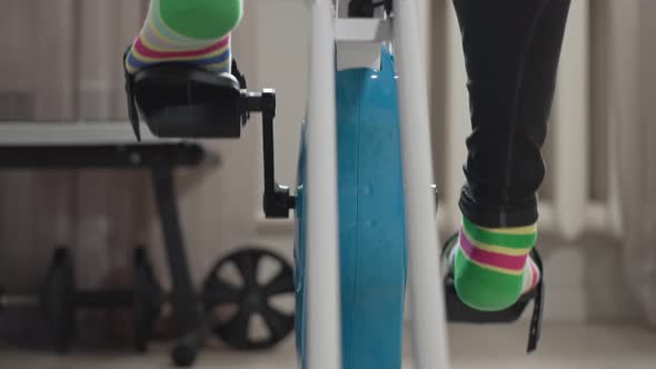Legs Pedaling an Exercise Bike at Home in a Room Closeup View