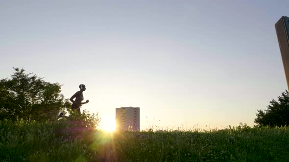 Slow motion shot of woman with headphones jogging on meadow at sunset