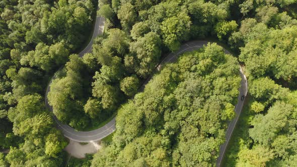 Aerial top shot of a double curve in a green forest - timelapse of a fast driving car from above thr