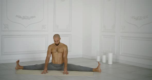 Male Yogi Is Sitting in Split Position in Hall and Meditating with Closed Eyes