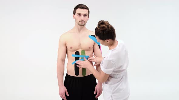 Female therapist applying kinesiology tape on a man's abdomen on the white background