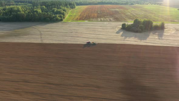 Tractor Plows Field Or Plants Seeds In Spring Against The Sun Rays At Sunset