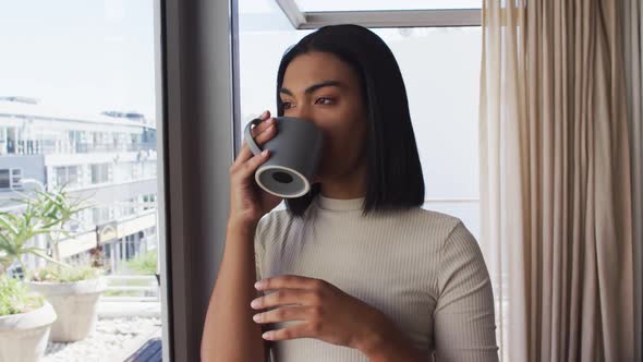 Mixed race gender fluid person drinking a cup of coffee and looking through window