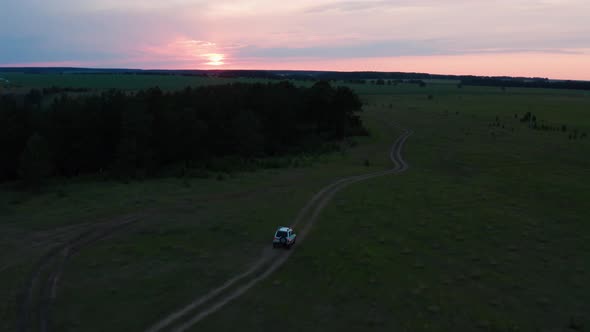 Aerial View of a Car Driving in Nature on a Field at Sunset