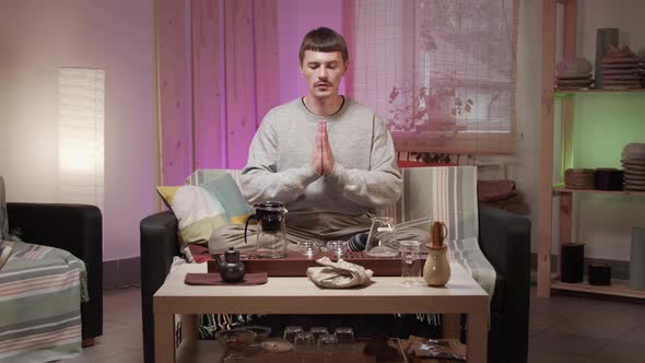 A Man in a Grey Sweater Prays with His Hands Folded During a Tea Ceremony Before Drinking Tea in His