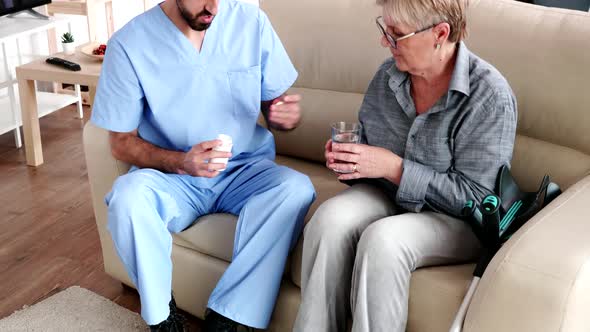 Male Nurse on Couch with Elderly Retired Woman Giving Her Medical Treatment in Retirement Home