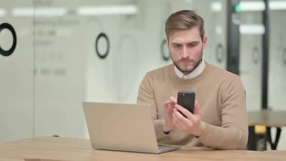 Creative Young Man Using Smartphone While Working on Laptop