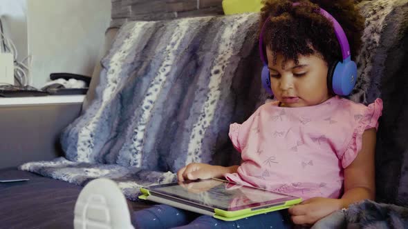 Little girl using tablet and listening to music on sofa