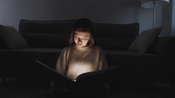 Night Time Portrait of Asian Female Sitting at Home on the Floor and Reading a Book Warm Light