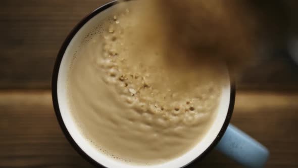 Pour Cane Sugar From Spoon Into Cup of Coffee with Milk