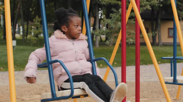 Alone Calm Sad African Children Ride on Round Swing in City Park