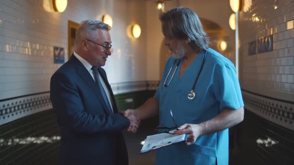 Practicing Doctor and Patient Shaking Hands Smiling at Clinic Corridor