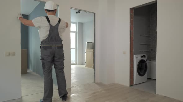 A Builder in Working Uniform Checks the Size and Quality of Doorways in a New Apartment