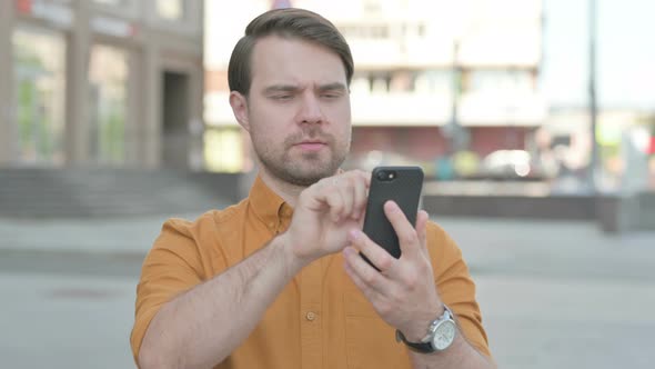 Young Man Browsing Internet on Smartphone Outdoor