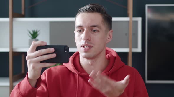 Portrait of Happy Man Making Facetime Video Calling with Smartphone at Modern Home Office, Waving at