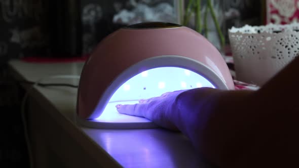 A Woman Dries Her Nails In An Ultraviolet Lamp. She Gives Herself A Manicure.