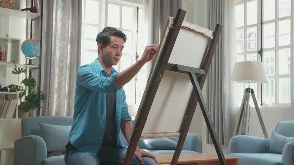 Asian Artist Man Holding Paintbrush And Mixing It With Colour Before Painting On The Canvas