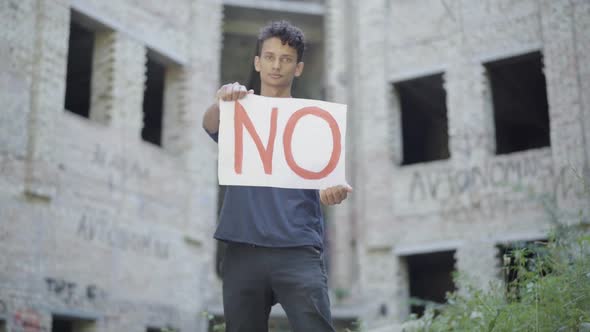 Portrait of Mixed-race Young Man Raising No Poster and Looking at Camera. Rack Focus Changes From