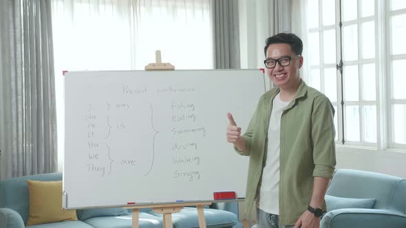 Asian Male Teacher Showing Thumbs Up Gesture And Smiling To Camera While Teaching English At Home