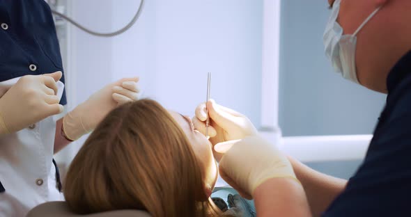 The Dentist Examines the Woman's Oral Cavity Using a Dental Mirror