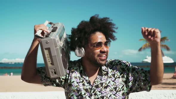 Happy Afro man having fun listening to music with headphones and boombox on the beach