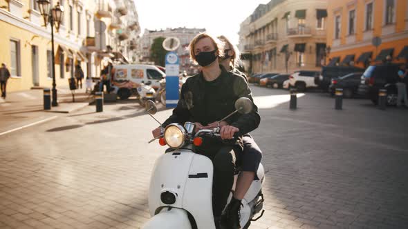 Happy Young Hipster Couple Riding a Vintage Scooter in City in Protective Masks During Pandemia of