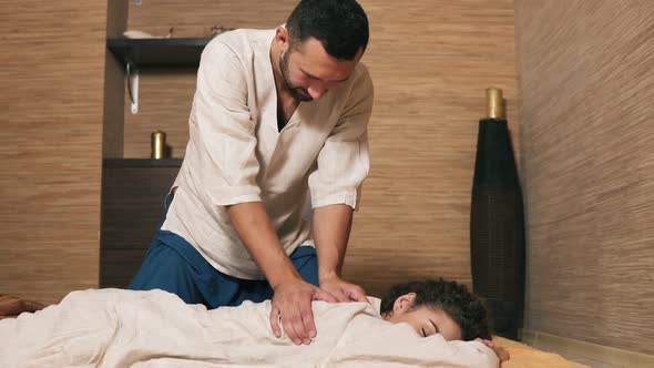 Male Thai Massagist is Treating Young Woman's Back and Shoulder