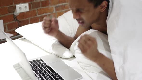 Financial Loss for African Man Working on Laptop Lying on Stomach