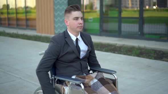 Young Businessman in a Suit in a Wheelchair. A Serious Man Is Riding in a Wheelchair Against a