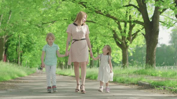 Wide Shot of Young Positive Mother Strolling Outdoors with Children. Cute Little Girl and Boy