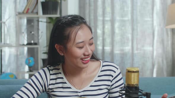 Close Up Of Asian Woman With Microphone Waving Hand And Speaking Before Playing A Guitar At Home