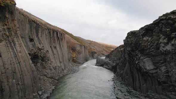 Drone flight through narrow Studlagil Canyon, Iceland above glacial river.