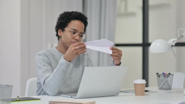 African Woman Making Paper Plane While Working on Laptop