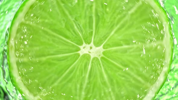 Super Slow Motion Detail Shot of Rotating Fresh Lime Slice and Splashing Water at 1000Fps alt