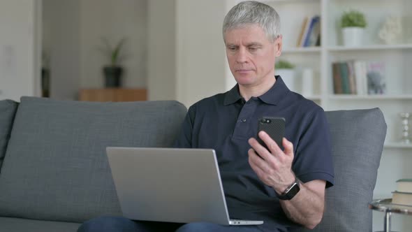 Hardworking Middle Aged Businessman Using Smartphone and Laptop 