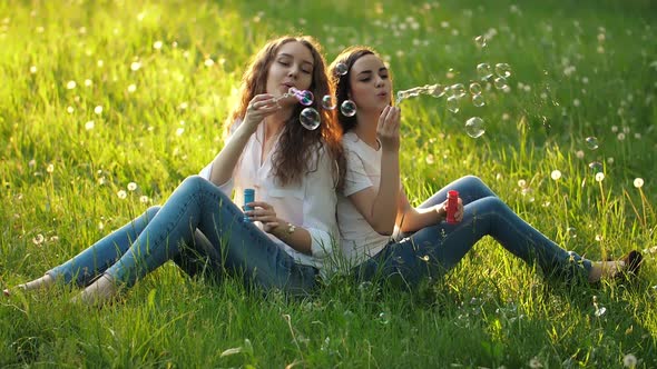Girlfriends Sitting on the Grass and Blowing Bubbles