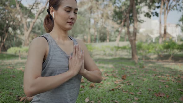 Young woman wearing earphones and sitting in lotus position in city park.