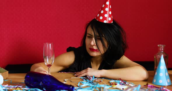 Young Woman with Red Rubbed Lipstick and Cap Wake Up in the Morning at Table in Messy Room After