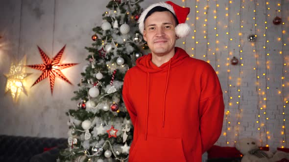 Young Handsome Man in Santa Hat on Background of Christmas Tree