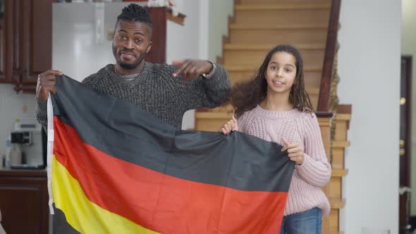 Joyful African American Father and Daughter Posing with German Flag Showing Thumbs Up Smiling