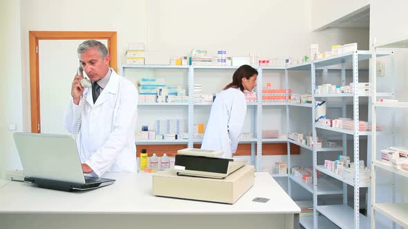 Pharmacist talking on the phone in a pharmacy with an other pharmacist